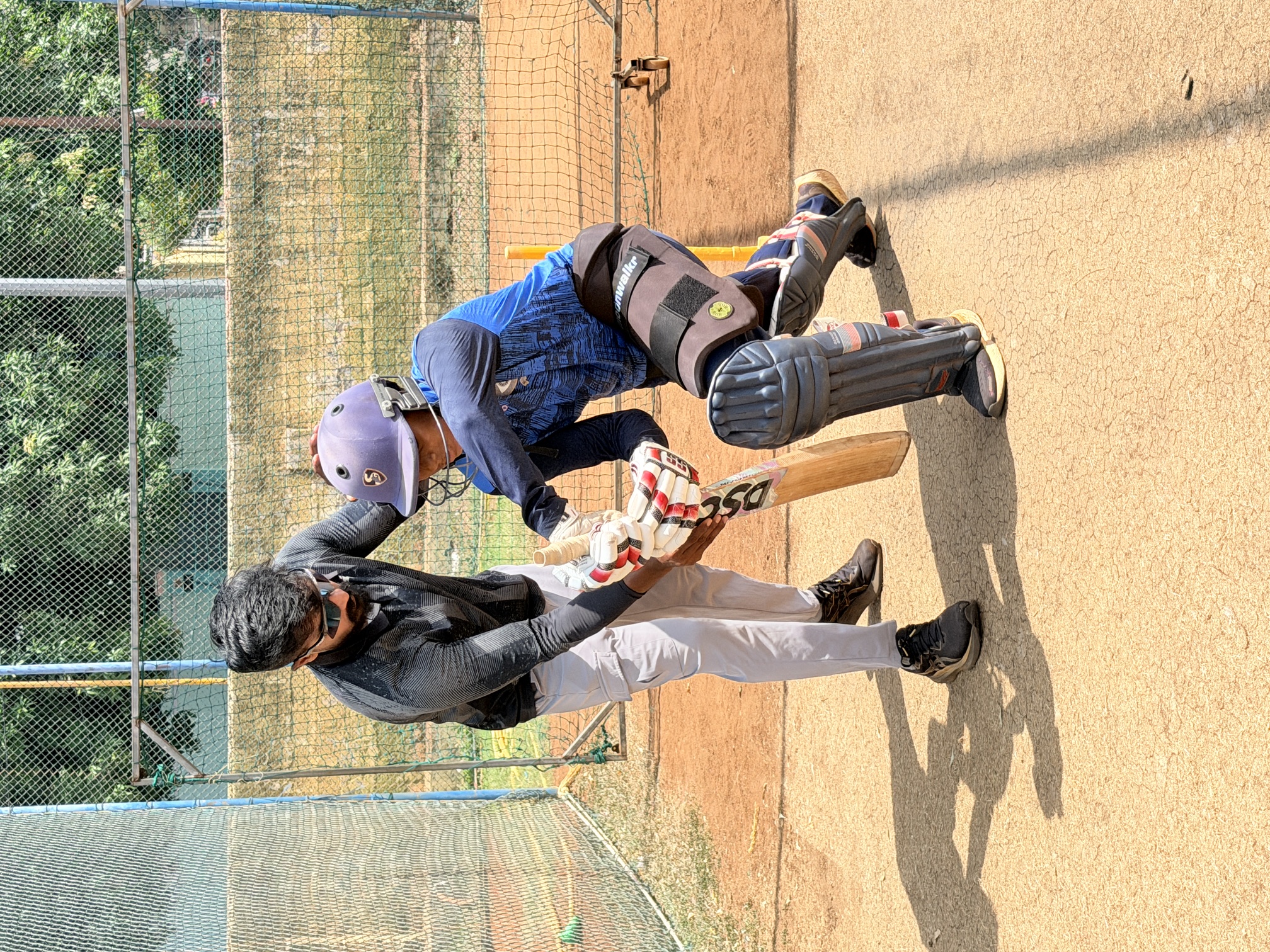 Coach guiding a young batter's stance in the practice nets