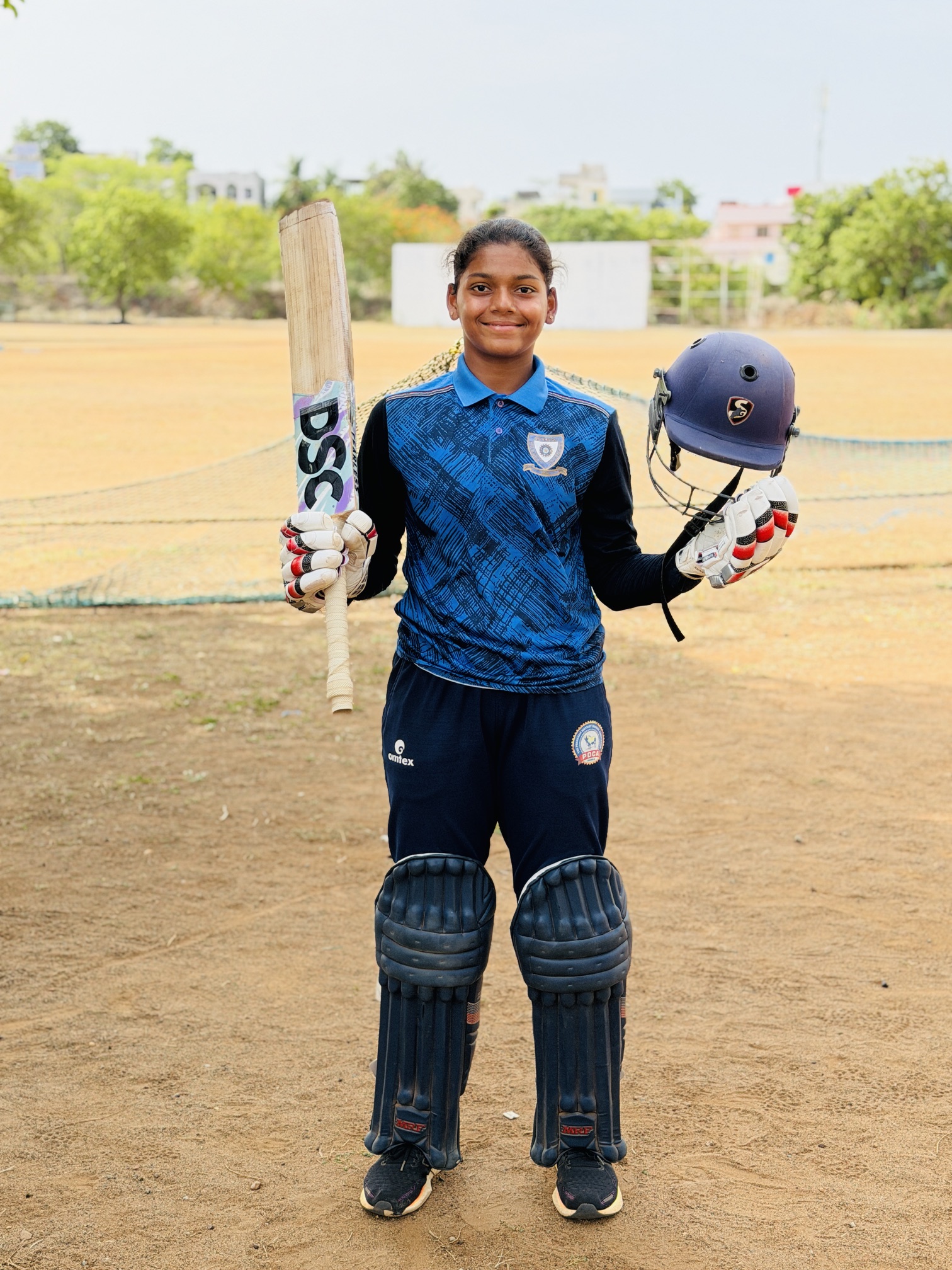 Young cricketer holding a bat and helmet at the academy ground