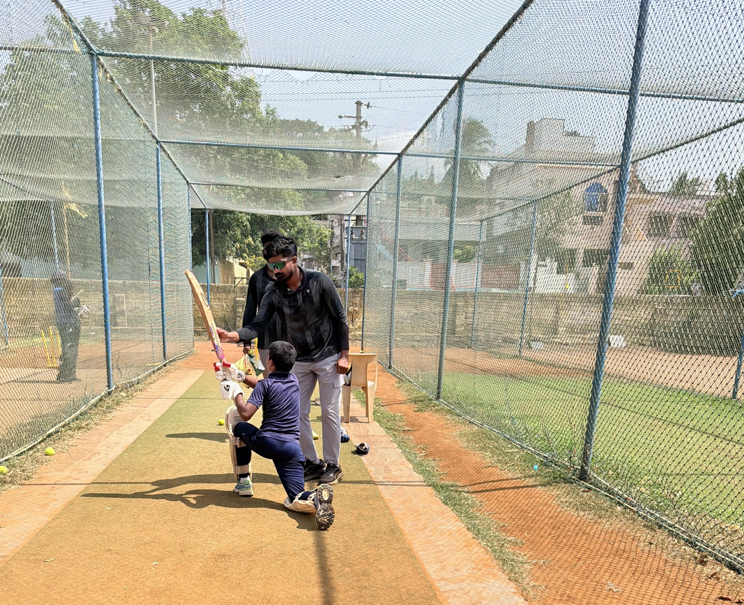 Coach demonstrating batting technique to a young player in the nets