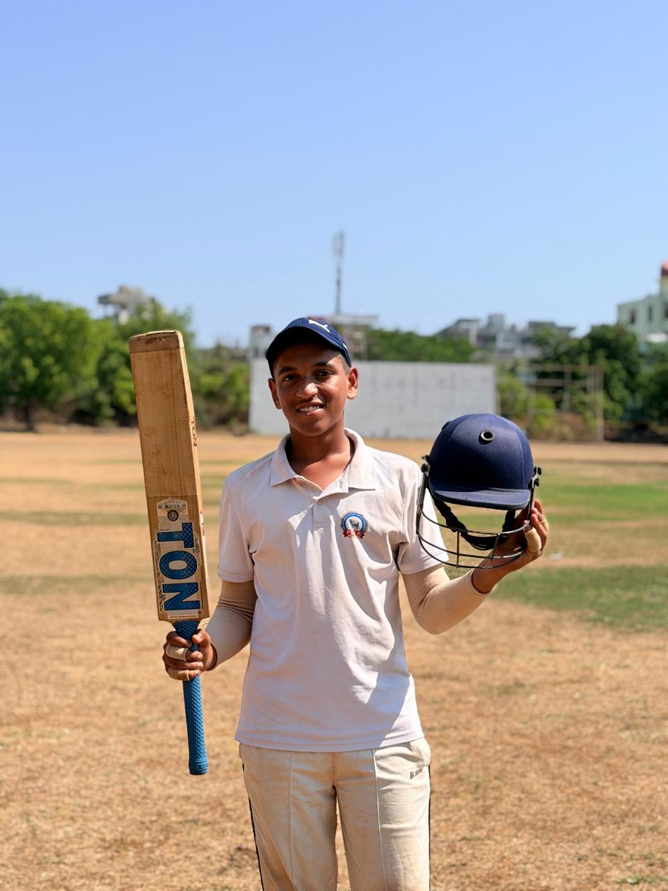 Young cricketer holding a bat and helmet at the academy ground